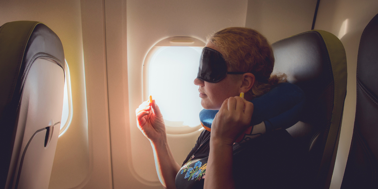 Kobieta w samolocie z opaską na oczy, poduszką i zatyczkami do uszu